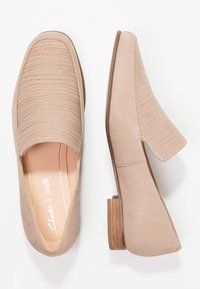 Mocassins beige à enfiler avec dessus texturé, côtés en cuir lisse, talon bas empilé et semelle intérieure rembourrée, présentant un design minimaliste.