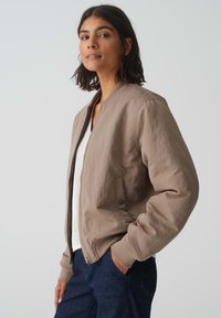 Giubbotto bomber marrone chiaro realizzato in tessuto morbido e texture, con chiusura zip frontale, polsini a coste e tasche laterali.