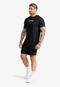 Svart kortärmad träningsskjorta med vitt logotyp, i kombination med svarta shorts och vita sneakers. Slitstark, lättviktig tyg med en åtsittande design.