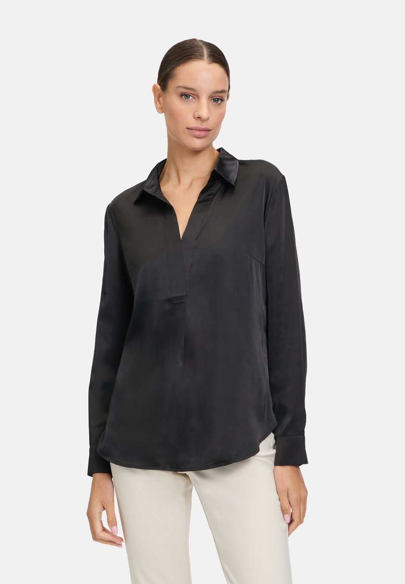 Zwarte satijnen blouse met lange mouwen en een v-hals, met een ontspannen pasvorm, subtiele glans en ronde zoom, gecombineerd met beige broek.