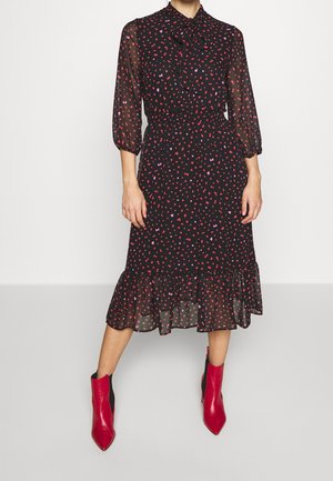 Robe noire avec de longues manches transparentes, motif de cœurs roses et violets, ourlet à volants, taille cintrée, associée à des bottines rouges ankle.