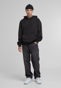 Sweatshirt à capuche noir avec un motif texturé, poche avant et poignets côtelés. Associé à un jean sombre et des chaussures de sport blanches.