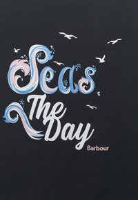 Černé tričko s stylizovaným textem "Seas The Day" v modré a růžové barvě, s malými bílými ptáčky nahoře a značkou "Barbour" v růžové barvě níže.