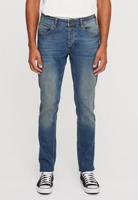 Mörkblå denimjeans med slim fit, bleknade detaljer, fem fickor och kontrasterande sömmar. Kombinerat med svartvita sneakers.