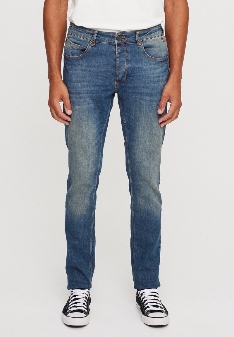 Mörkblå denimjeans med slim fit, bleknade detaljer, fem fickor och kontrasterande sömmar. Kombinerat med svartvita sneakers.