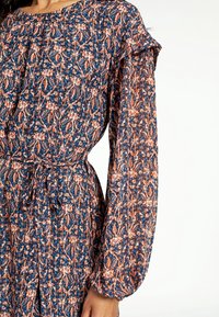 Robe fleurie bleu marine avec des motifs orange et blancs. Caractérisée par des manches longues bouffantes et une taille à cordon pour une silhouette ajustée.