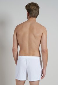 Witte katoenen boxershorts met een elastische tailleband, van achteren getoond, op een persoon met kort, lichtbruin haar tegen een neutrale achtergrond.