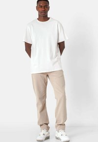 Camiseta blanca de algodón con mangas cortas, pantalones beige texturizados y zapatillas blancas estampadas, estilizadas en un ajuste relajado.