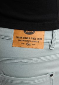 I pantaloni di jeans azzurri chiari presentano un'etichetta in pelle con il marchio "Teiro" e la scritta "Denim Driven Since 1989" in rilievo. Cuciture a vista sui tasconi.