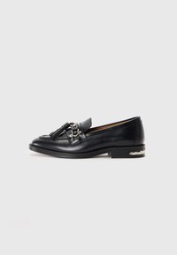 Loafer en cuir noir avec des franges et un détail de boucle en métal à l'avant, talon bas avec accent en argent, sur fond blanc uni.