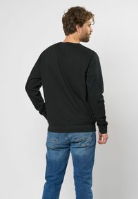 Zwarte sweatshirt met lange mouwen en een ronde hals, met een geribbelde zoom. Gecombineerd met lichtblauwe denim jeans.