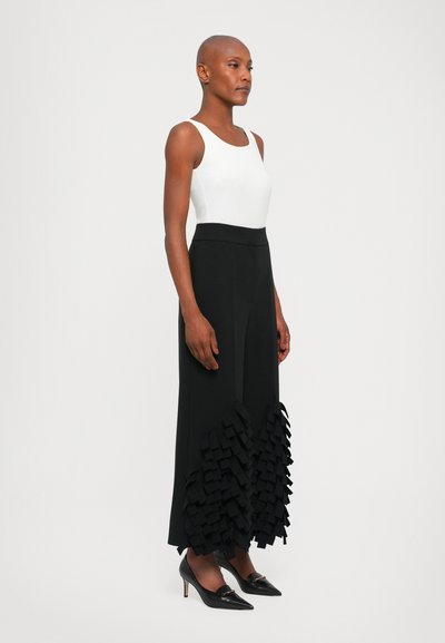 Pantalones anchos negros con un dobladillo rizado texturizado, combinados con una camiseta ajustada blanca y tacones negros puntiagudos. Tecido suave, líneas limpias.