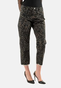 Jeans recortados de patrón negro y marrón con pierna recta; cuenta con un cierre de botón y un dobladillo deshilachado, combinados con tacones altos negros.