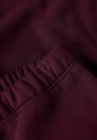 Bordo tkanina koja prikazuje glatku teksturu, s detaljem naboranog struka i ravnim šavom. Materijal izgleda mekano i rastezljivo.