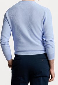 Světle modrý pletený svetr s kulatým výstřihem a žebrovanými manžetami, zdobený texturovaným vzorem; v kombinaci s tmavými kalhotami.