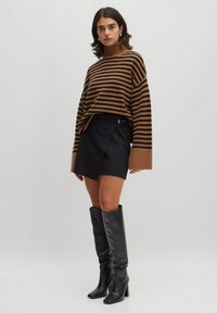 Bruine en zwarte gestreepte coltrui met brede mouwen, gecombineerd met een zwarte mini-jurk met een zijknop. Zwarte laarzen tot de knie.