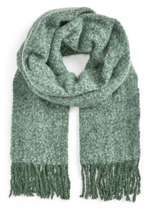 Écharpe tricotée verte, épaisse et douce, avec une texture duveteuse et des franges aux extrémités, pliée en boucle lâche sur fond blanc.