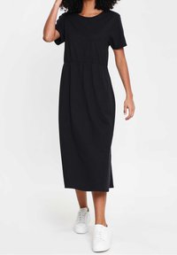 Robe midi en coton noire avec manches courtes, taille cintrée et coupe décontractée. Portée avec des baskets blanches, elle présente un col rond simple.