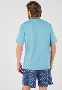 Lichtblauw T-shirt met korte mouwen en ronde hals, gecombineerd met marineblauwe shorts met een wit en rood ankerpatroon.