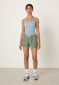 Canotta a righe blu abbinata a pantaloni corti verdi testurizzati, con vita regolabile. Il modello indossa calze bianche e scarpe da ginnastica grigie.