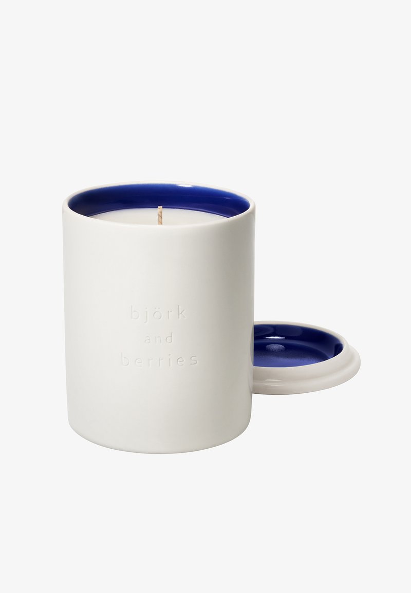 Weißer Keramikkerzenbehälter mit dunkelblauem Innenraum, einem Docht in der Mitte und einem passenden Deckel daneben gelegt.