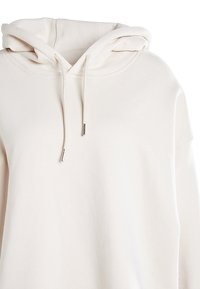 Felpa pullover color avorio con cappuccio e lacci con punte in metallo, tessuto morbido e vestibilità ampia.