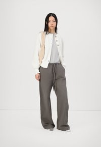 Cardigan en tricot blanc avec des boutons en bois, t-shirt gris, pantalons gris amples et chaussures argentées. Le mannequin porte un sac tote beige.