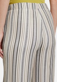 Gestreepte wijde broek met een mix van crème, zwart en beige tinten, met een textuurstof en een elastische tailleband.