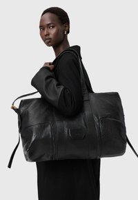 Black leather duffel bag with textured finish, featuring sturdy handles and a gold-tone zipper. Designed with a rectangular shape and side pockets.