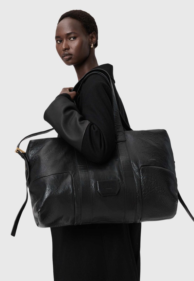Black leather duffel bag with textured finish, featuring sturdy handles and a gold-tone zipper. Designed with a rectangular shape and side pockets.