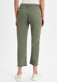 Pantaloni cropped verde oliva con orlo sfrangiato, due tasche posteriori e un tessuto testurizzato. Indossati con sneakers bianche, dotate di un'etichetta beige in vita.