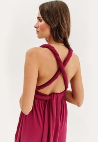 Bordová šaty s prekrútenými ramienkami, odhaleným chrbtom a viazaním v páse. Vyrobené z mäkkého materiálu s voľným strihom a hladkou textúrou.
