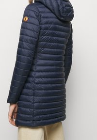 Marine pufferjas met een capuchon, voorzien van doorgestikte panelen, lange mouwen en een logo patch op de linkerschouder, gemaakt van glad, lichtgewicht materiaal.