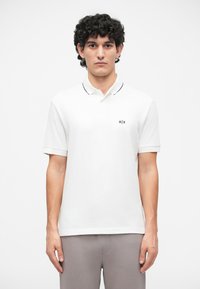 Cămașă polo albă cu garnitură neagră la guler și logo pe partea stângă a pieptului. Mâneci scurte, realizată dintr-un material fin din bumbac. Design simplu.