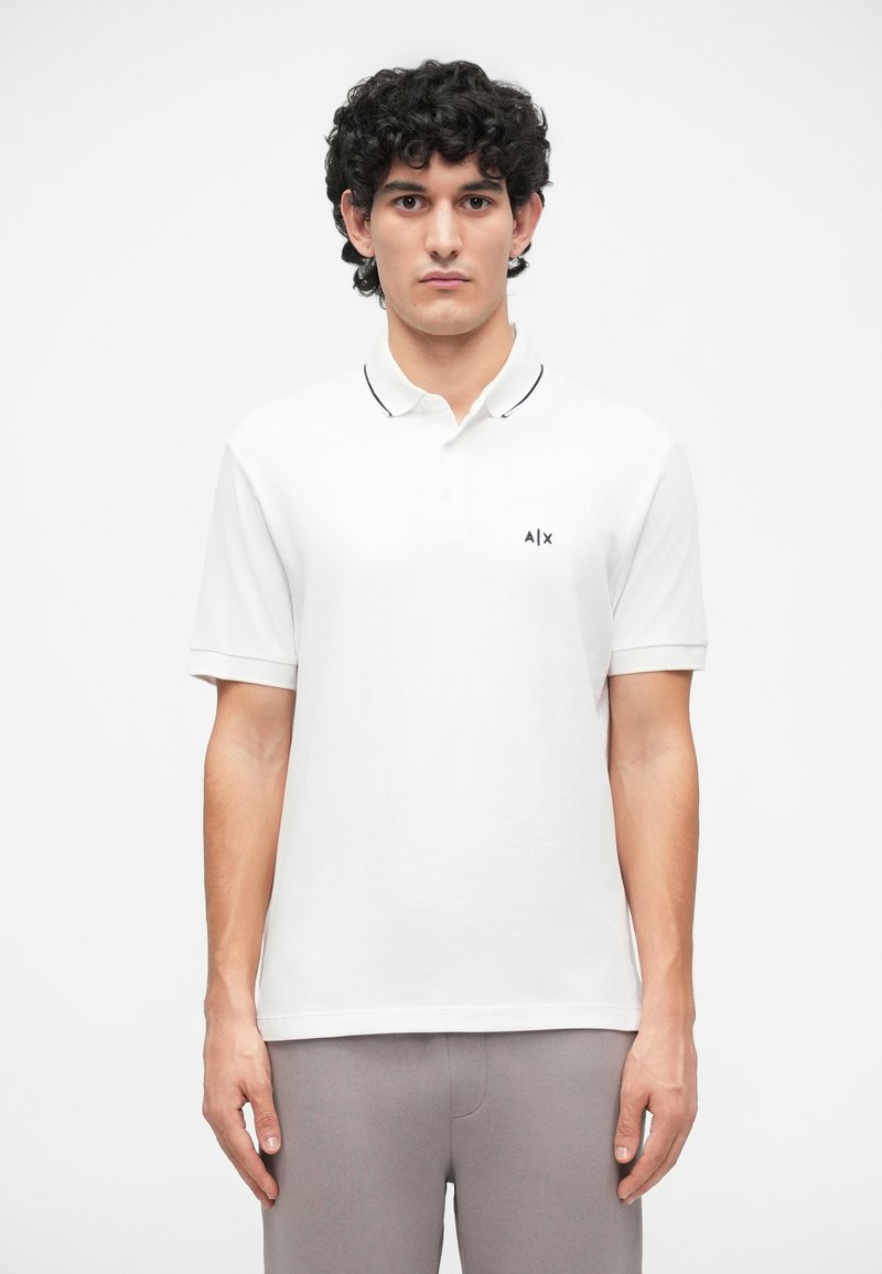 Cămașă polo albă cu garnitură neagră la guler și logo pe partea stângă a pieptului. Mâneci scurte, realizată dintr-un material fin din bumbac. Design simplu.