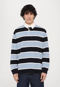 Langermet polo-skjorte i blå, svart og hvite striper. Har en kontrastfargehvit krage og en liten merkedesign på brystet.