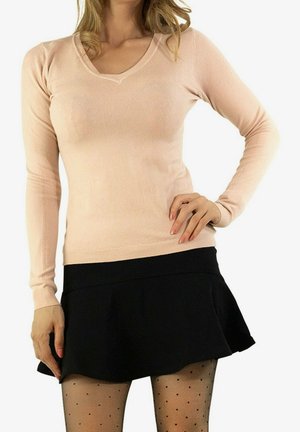 Pull long rose clair à manches longues avec un col en V, présentant une coupe ajustée et un ourlet côtelé. Porté avec une jupe noire évasée et des collants à pois.