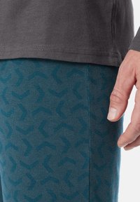 Gray t-shirt paired with teal patterned pants featuring a geometric design. Close-up of fabric texture and fit near the waist and hand.