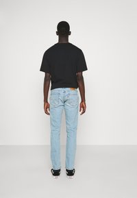 Jeans de mezclilla de color azul claro con un corte recto clásico, que presentan bolsillos traseros y una etiqueta de cuero marrón en la cinturilla, combinados con una camiseta negra.