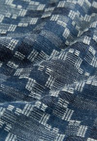 Tejido azul oscuro con un patrón texturizado de cuadrados y rayas entrelazados en blanco, mostrando una superficie tejida y ligeramente elevada.