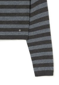 Jersey de rayas en gris oscuro y azul claro, con cuello redondo y un sutil brillo. Incluye un pequeño logo metálico cerca del dobladillo.