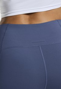 Granatowe legginsy sportowe o gładkiej fakturze, z płaskimi szwami i logo nadrukowanym w pobliżu pasa.