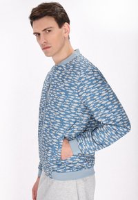 Light blue bomber jacket featuring a fish pattern in white, with ribbed cuffs and collar, and side pockets. Modern, streamlined design.