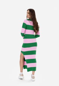 Abito in maglia con strisce orizzontali verdi e rosa, maniche lunghe e uno spacco alto sulla coscia da un lato. Abbinato a sneakers bianche.