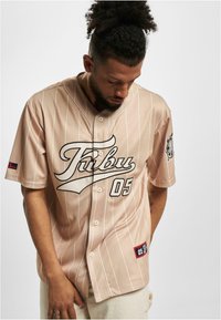 Jerseu de baseball bej cu dungi, text logo negru "Tribu," numărul "05" și detalii cu patch. Mâneci scurte, deschidere cu nasturi, material ușor.