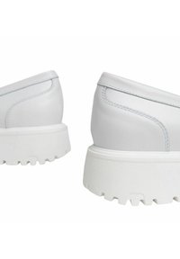 Sneakers bianchi con un design elegante, finitura opaca liscia, suola spessa e testurizzata, e dettagli di cucitura discreti sulla parte superiore.