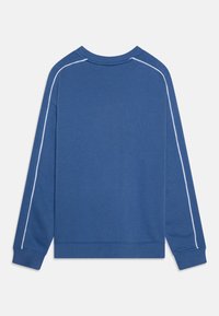 Blå genser med lange ermer, ribbestrikkede mansjetter og rund hals. Har hvite piping langs skuldersømmene. Lett og glatt stoff.