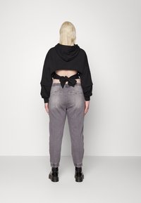 Kuttet svart hettegenser med et utskåret bakstykket knyttet i en sløyfe; paret med lys grå, litt slitt høytlivtejeans og svarte støvler.