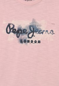 Lyserød bomulds T-shirt med en blå akvarel effekt og teksten "Pepe Jeans London" i kontrasterende mørkeblå. Rund halsudskæring.