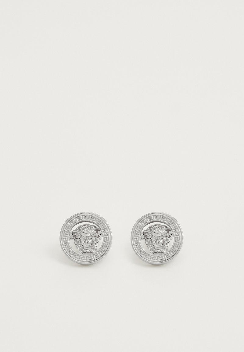 Pendientes de plata redondos con un motivo de león en relieve, enmarcados por un patrón geométrico de clave griega. Textura lisa con acabado pulido.